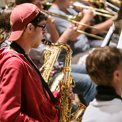 Man playing a saxophone with a line of people playing trumpets in the background
