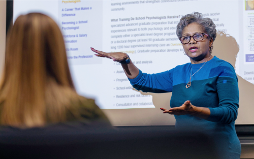 A professor lecturing in front of a projector screen