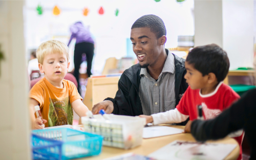 a student sitting at a table doing crafts with two children