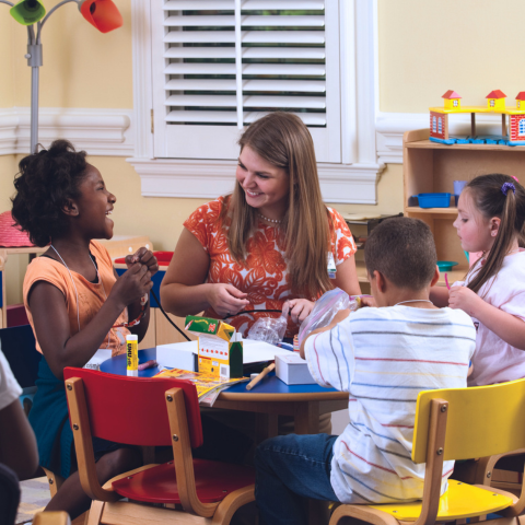 Woman at a colorful kids table working with three small children
