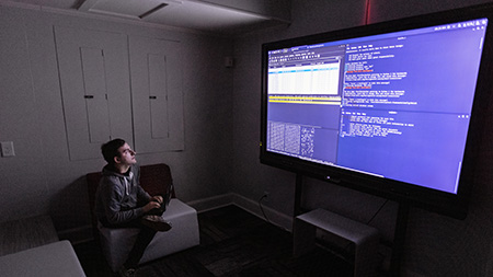 A student writing code on a large monitor