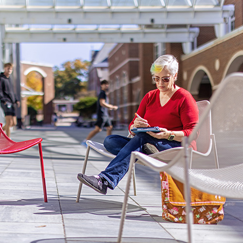 A smiling student in a rocking chair with a laptop