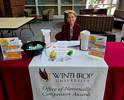 the ONCA director sitting behind a table with a logo on it during a tabling event.
                           Flyers and brochures are set up on the table