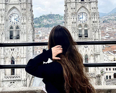 a girl standing near a fence looking out over a cathedral and city
